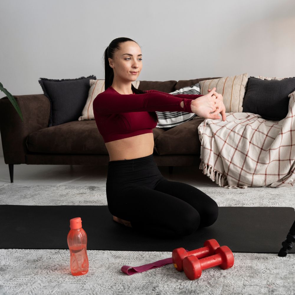 Woman exercising with dumbbells on a mat in a living room.
